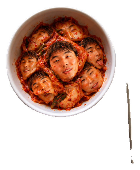 A white ceramic bowl of red kimchi with six grinning faces tucked among the cabbage leaves
